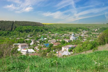 Ukrayna 'nın Ternopil bölgesinde yemyeşil ve yuvarlanan tepeler arasında yer alan Budaniv kasabasını bir kale tepesinin avantajlı noktasından gösteren manzara.