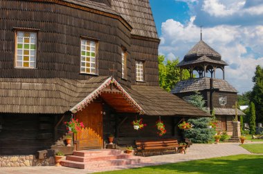 Yükseliş Kilisesi 'nde ahşap duvarlar ve çatılar, çiçeklerle süslenmiş ayrı bir ahşap çan kulesi sergileniyor, Ukrayna' nın Chortkiv kentinde bir yaz gökyüzüne karşı kuruluyor.