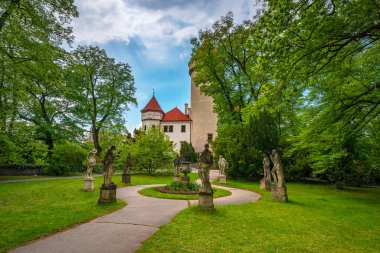 Yuvarlak kulesi ve kırmızı çatısı olan Konopiste kalesinin manzarası. Etrafı, klasik heykeller ve dolambaçlı bir patikayla süslenmiş yemyeşil bir parkla çevrili. Çek Cumhuriyeti 'nde Benesov yakınlarında yer almaktadır.