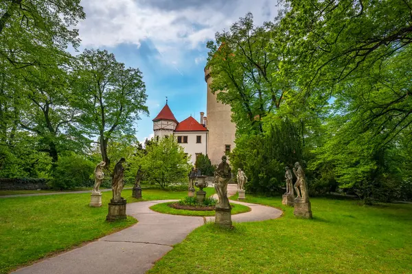 Yuvarlak kulesi ve kırmızı çatısı olan Konopiste kalesinin manzarası. Etrafı, klasik heykeller ve dolambaçlı bir patikayla süslenmiş yemyeşil bir parkla çevrili. Çek Cumhuriyeti 'nde Benesov yakınlarında yer almaktadır.
