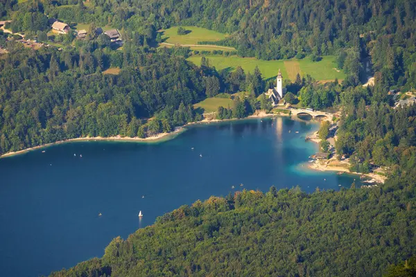 Bohinj Gölü 'nün manzaralı güzelliğini Vaftizci Aziz John Kilisesi, büyüleyici bir köprü ve bereketli ormanların arasında süzülen sakin sularda süzülen yelkenliler ile yakalıyorum.