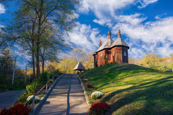 Wooden Cossack Church of Protection of Holy Mother of God rising on green hill in Monastyrok tract near Kaniv city in Cherkasy Oblast, Ukraine, on sunny autumn day with blue sky and white clouds