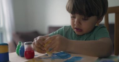 Evde boya yapmak için boya fırçası kullanan küçük bir çocuk. Evde çocuk yaratıcılığı sanatsal aktivitesi. Çocuk boyama