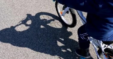 Bisikletli çocuk dışarıda bisiklet sürüyor. Küçük çocuk bisiklet sürerken gölgeler yerde.