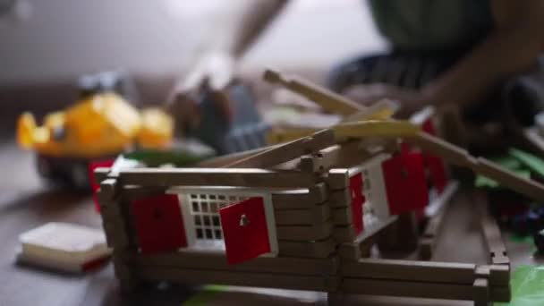 一个小男孩用拖拉机推土机摧毁了木制的房子玩具 男婴驱逐舰在房间里玩耍 — 图库视频影像