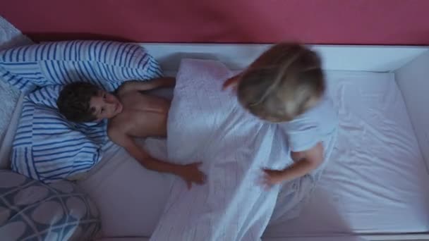 孩子们跳上床去了快乐的兄弟姐妹们在羽绒被下垂涎 — 图库视频影像