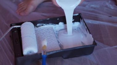  Kapalı el beyaz boyayı silindir ile tepsiye döküyor.