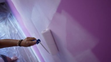 Mor duvara beyaz renk uygulayan yakın plan boya silindiri. Ev onarımı yapan kişi