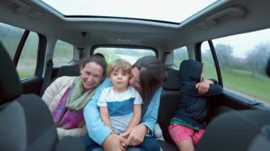 Arabanın arka koltuğundaki mutlu insanlar el sallıyor ve birlikte gülüyorlar. Aile araçla yol kenarında seyahat ediyor.