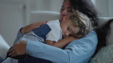 Anne ve çocuğu kanepede birbirlerine sarılıyorlar. Samimi, otantik bir anne, uykulu oğlunu kollarında okşuyor. Aile sevgisi ve sevgi