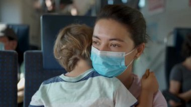  Anne ve çocuk trenle seyahat ediyor. Anne, ameliyat maskesi takıyor. Virüse karşı korunuyor.