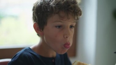 Bir çocuk sabah kahvaltısında brioche ekmeği yiyor. Ergenlik yüzünden çocuğun yüzü kapanır ve karbonhidrat yer.