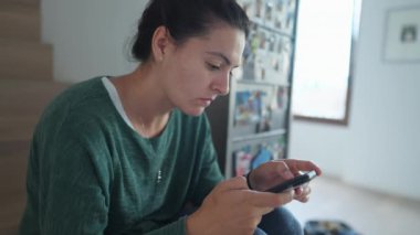 Bir kadın evde akıllı telefon cihazına bakıyor. Gerçek hayatta yetişkin biri cep telefonu ekranına bakıp merdivenlerde oturuyor.