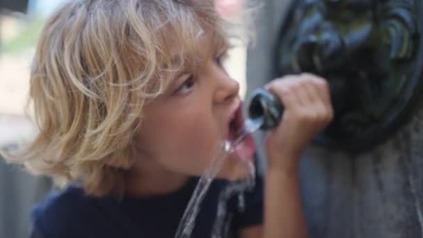 公共の噴水から一人の金髪の子供が飲んでいる 都市部のストリート蛇口からの子供の飲み物 — ストック動画