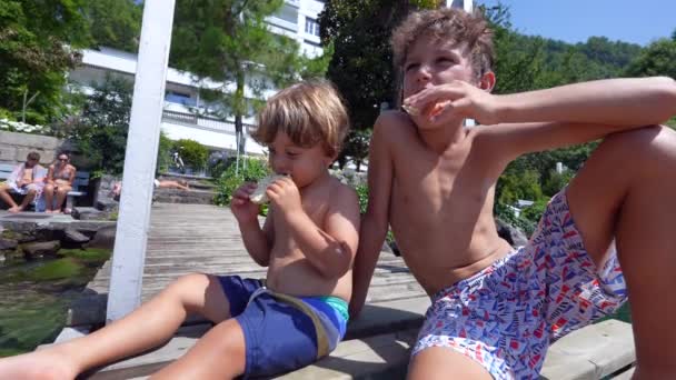 Два Мальчика Зависают Озерном Пирсе Поедая Крекеры Дети Сидят Палубе — стоковое видео