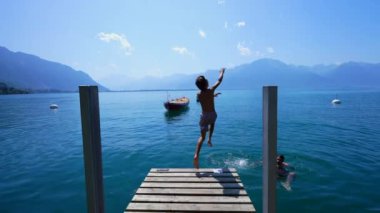 Genç çocuk gölde koşuyor ve arka planda dağlarla Cenevre Gölü 'ne atlıyor. Çocuk yaz tatillerinde eğleniyor.