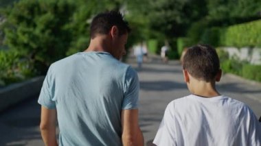Babanın arkasında, genç oğluyla yeşil parkta yürüyor. Ebeveyn ve küçük çocuğun kaynaşma anı. Aile ilişkisi.