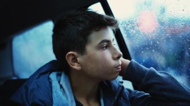 Yağmurlu bir günde camdan dışarı bakan üzgün bir genç çocuk. Düşünceli çocuk.