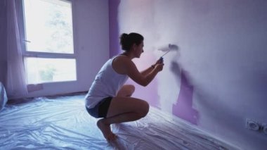  Boya silindirli biri. Kadın evi yeniliyor. Mor duvarı beyaz renklerle boyuyor. ÇEVİR 