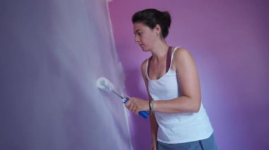  Boya silindirli biri. Kadın evi yeniliyor. Mor duvarı beyaz renklerle boyuyor. ÇEVİR 