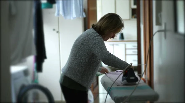 洗濯室での年配の女性のアイロン掛け服 率直な家庭主婦 — ストック写真