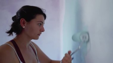 Boya silindirli biri. Kadın evi yeniliyor. Mor duvarı beyaz renklerle boyuyor. ÇEVİR 