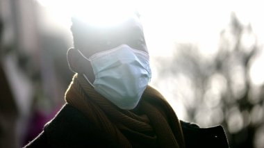African man standing wearing covid-19 face mask looking at camera with sunlight flare