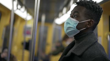 African man standing in subway metro wearing coronavirus mask underground