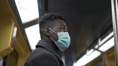 African man standing in subway metro wearing coronavirus mask underground commute