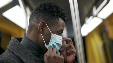 African man standing in subway metro wearing coronavirus mask underground commute