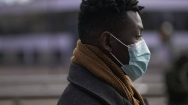 African man walking in city during pandemic times wearing covid mask