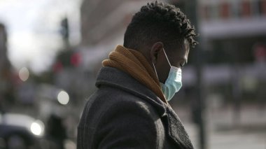 African man walking in city during pandemic times wearing covid mask