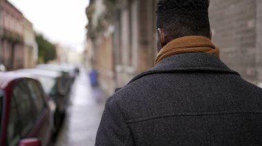 Şehir merkezindeki kaldırımda yürüyen Afrikalı bir adamın arkası. Afrikalı kişi bakış açısı
