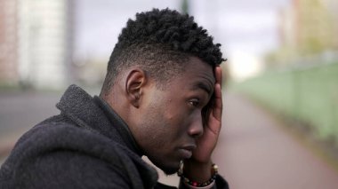 Anxious young black man suffering emotional pain sitting on sidewalk in street