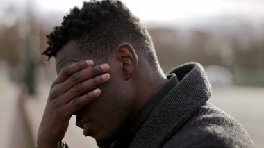 Duygusal acı çeken endişeli genç siyahi adam kaldırımda oturuyor.
