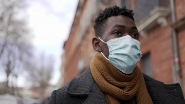 Black African man walking wearing covid surgical face mask in city sidewalk, tracking shot