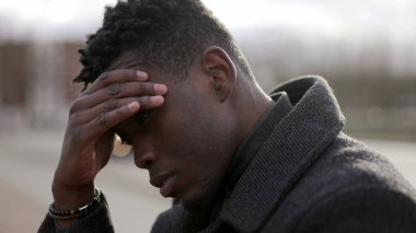 Duygusal acı çeken endişeli genç siyahi adam kaldırımda oturuyor.