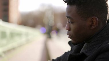 Duygusal acı çeken endişeli genç siyahi adam 2nci sokakta kaldırımda oturuyor.
