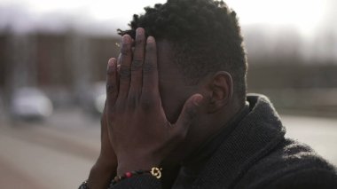 Duygusal acı çeken endişeli genç siyahi adam kaldırımda oturuyor.