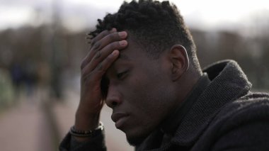 Anxious young black man suffering emotional pain sitting on sidewalk in street