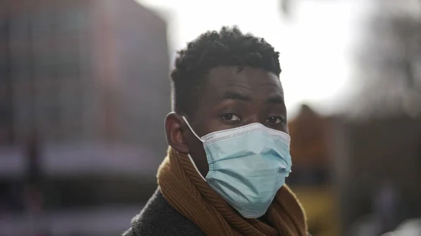 Black African man wearing covid-19 surgical face mask standing outside in city portrait