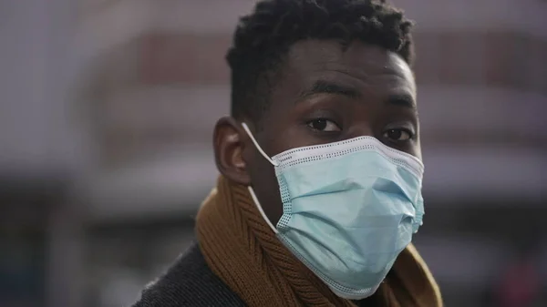 Black African man wearing covid-19 surgical face mask standing outside in city portrait