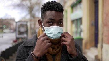 Black man putting covid face mask while walking in city outside in the cold winter season