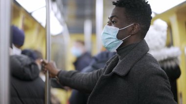 Black man holding bar at subway metro wearing covid surgical face mask prevention