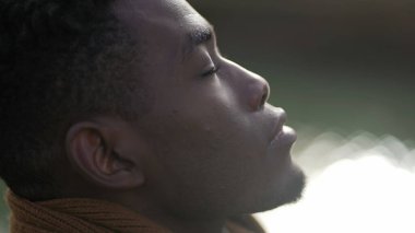 Black man taking a deep breath outside and opening eyes looking up at sky smiling feeling free