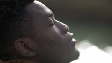 Black man taking a deep breath outside and opening eyes looking up at sky smiling feeling free