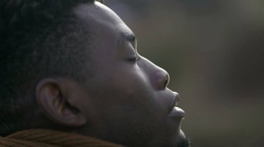 Black man taking a deep breath outside and opening eyes looking up at sky smiling feeling free