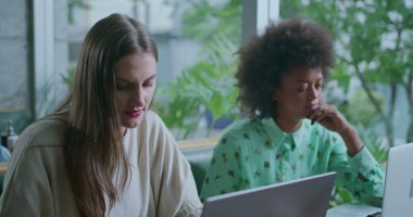 Dizüstü bilgisayarların önünde çalışan iki genç kadın. Kahve dükkanında iş birliği yapan bayan iş arkadaşları.