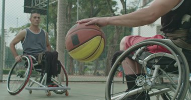 Belden aşağısı felçli bir erkek sporcu dışarıda meslektaşından top alıyor. Dışarıda spor salonunda basketbol oynayan iki engelli sporcu. Spor ve sakatlık kavramı