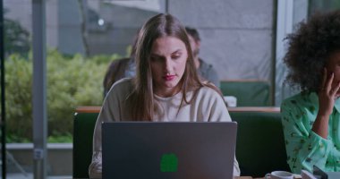 Uzaktan kumandalı bir kafede çalışan konsantre genç bir kadın arkadaşlarıyla birlikte masada oturan dizüstü bilgisayarın önünde.